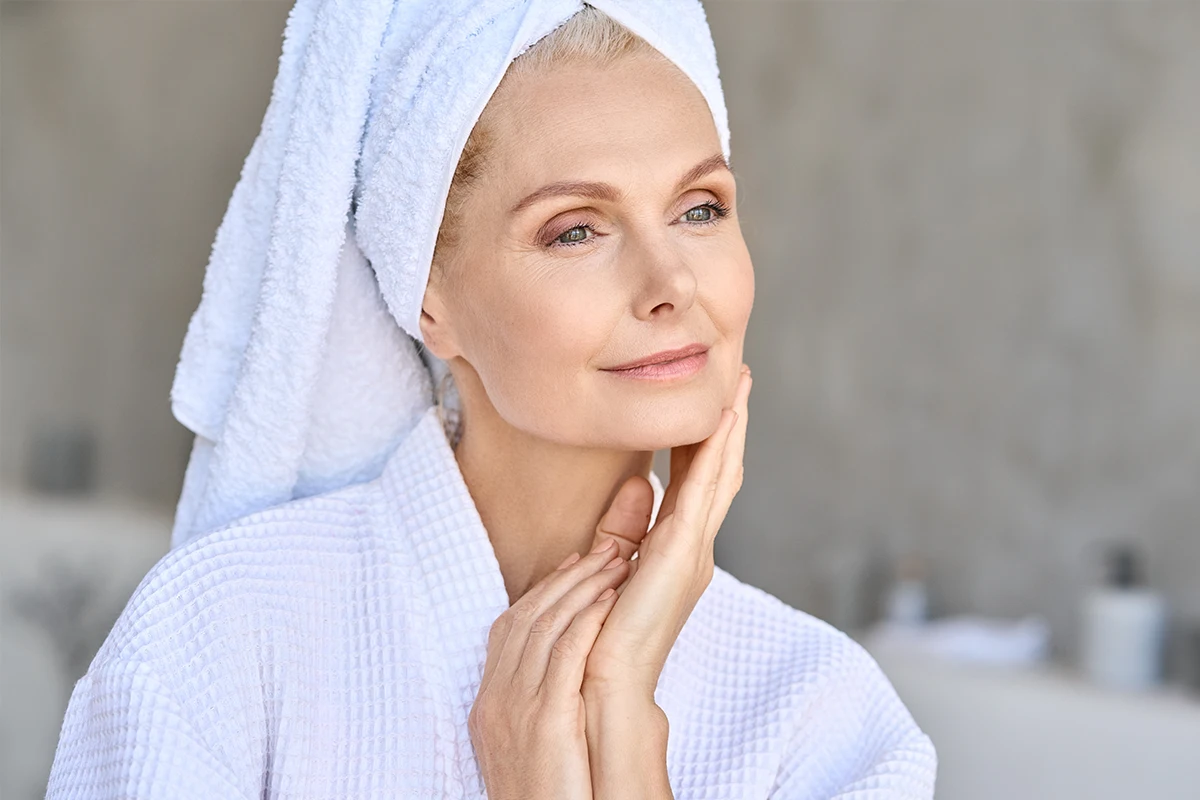 Woman in bathrobe touching her jawline after facelift surgery before menopause in Cincinnati