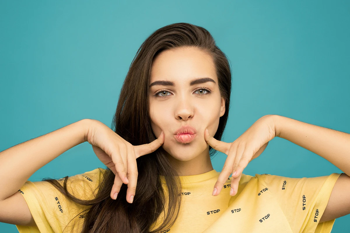 Attached, use Alt-Tag: woman puckering lips and touching cheeks, illustrating lip filler results and considerations about permanence